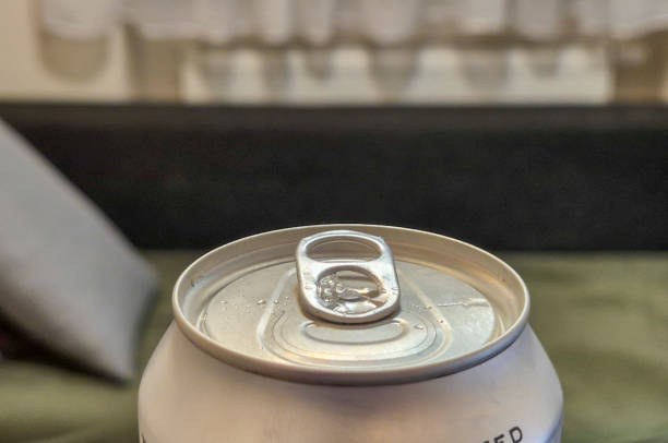 Close-up of a soda can lid with a pull-tab, showing condensation and a blurred background. A refreshing drink perfect for festive gatherings.