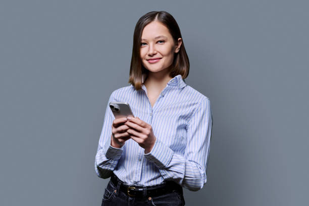 istock Young smiling woman using smartphone looking at camera in grey background 2190735082