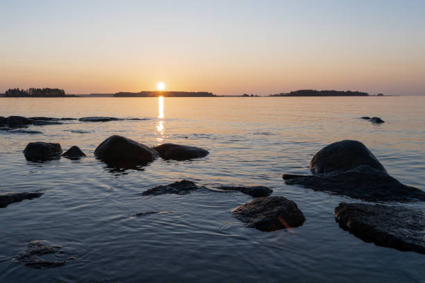 Sunrise over the islands. Morning. Clear clear sky. Calm water. Rocks are sticking out of the water. The water is separated from the sky by a horizon line on which other islands can be seen. The sun is rising over the islands.