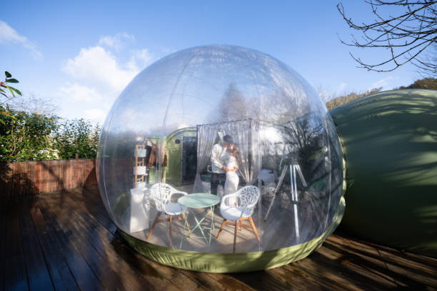 istock Romantic couple embracing inside transparent bubble hotel room, featuring minimalist furnishings, positioned on wooden deck, sharing intimate moment during secluded vacation 2190738274