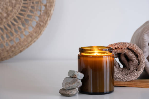 istock A soothing composition featuring an amber candle jar with a glowing flame, placed alongside rolled towels in beige shades 2190738763