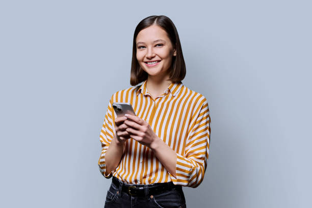 istock Young smiling woman using smartphone looking at camera in grey background 2190738905