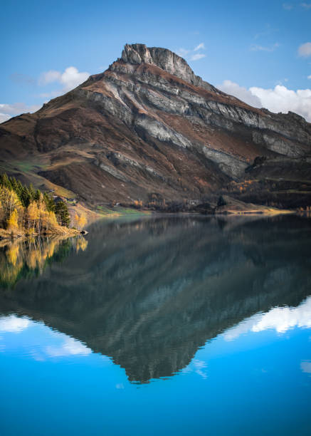 Landscape photography of Rocher du Vent reflecting in Lac de Roselend on a sunny autumn day, vertical