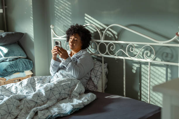 istock Woman sitting in bed using a smartphone during morning light 2190744713