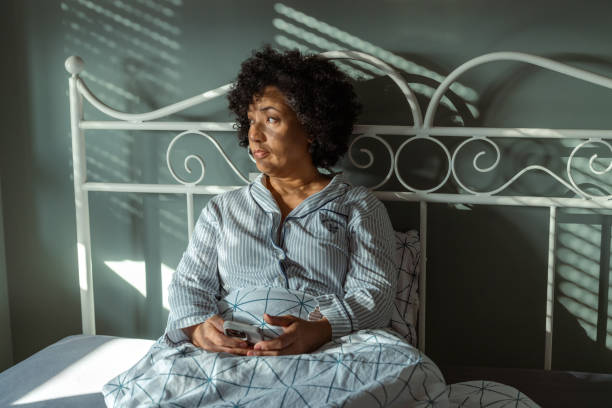 istock Woman sitting on bed looking away while holding a smartphone 2190744715