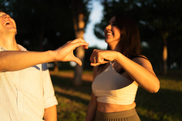 Happy couple making a heart shape with their hands, enjoying a romantic moment in a park at sunset