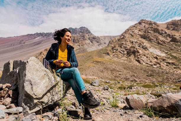 Tourist woman charging mobile phone using solar panel\n and lookig at view on a mountain, in Cajon del Maipo, Chile