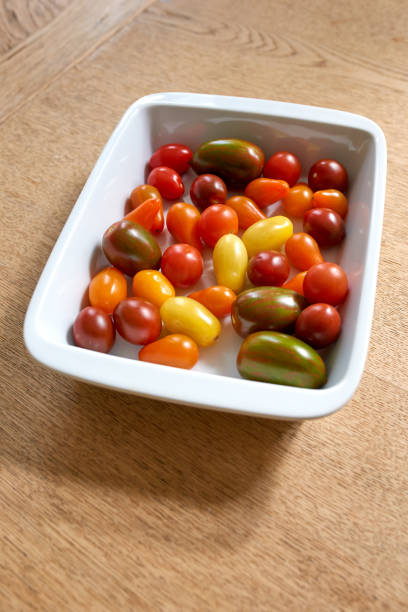 Colorful variety of cherry tomatoes in a white dish on a wooden table, showcasing fresh produce from Mallorca, Spain. Highlighted are vibrant colors and natural textures, promoting organic farming and Mediterranean cuisine.