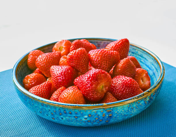 A bowl of ripe, fresh strawberries displayed against a vibrant blue backdrop, illustrating natural beauty. Photographed in Mallorca, Spain, this image highlights the vivid colors of fresh produce and nature.