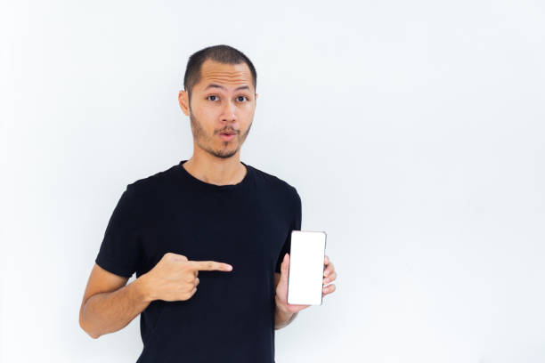 istock Young men with black empty shirt  smiling and pointing to phone with white screen template mockup 2190766843