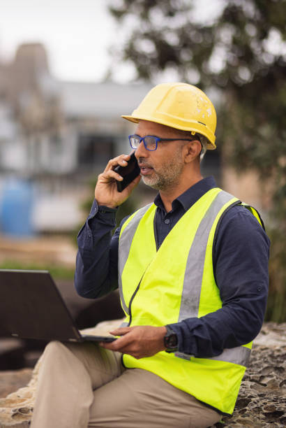 istock Engineer in safety vest and hard hat making a call on his phone while on site 2190768474