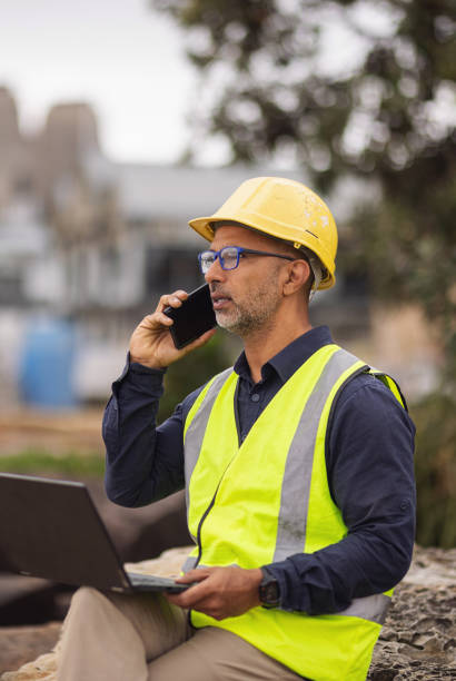 istock Engineer in safety vest and hard hat making a call on his phone while on site 2190768492
