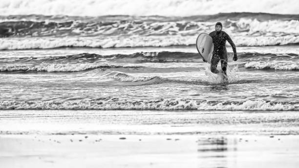 The Pacific Rim National Park in British Columbia on April 28, 2024: Young male surfer returning after a session at Pacific Rim National Park on Vancouver Island, British Columbia