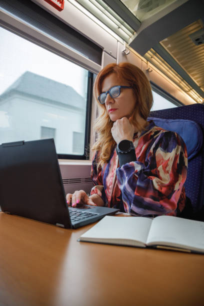 istock Beautiful woman with eyeglasses riding train by day and using laptop, commuter line 2190780430