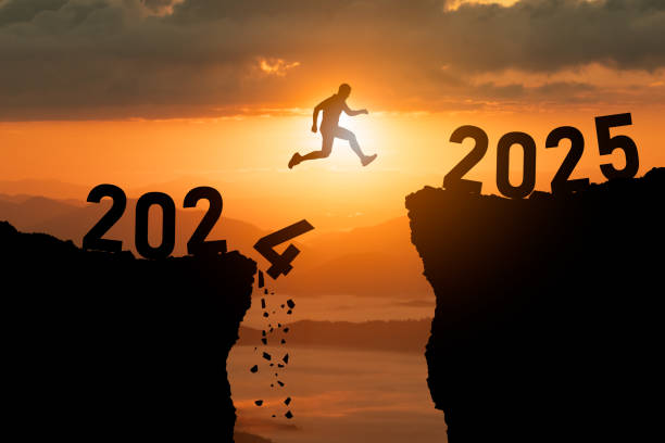 istock A determined runner leaps over a chasm labeled 2024 toward a bright future represented by 2025, symbolizing ambition, change, and progress at sunset. 2190781270