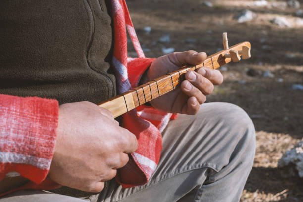 A young man is playing a traditional Turkish musical instrument, the Cura, in the forest.