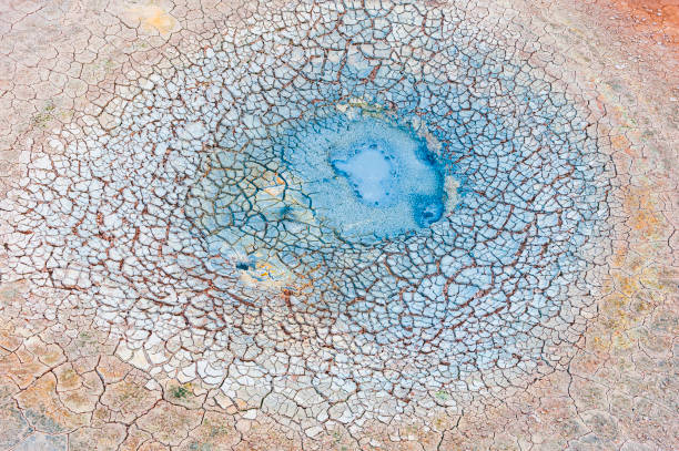 A circular blue pool is surrounded by dry, cracked earth in a barren landscape. The scene captures the unique patterns of drought-affected soil under bright sunlight.