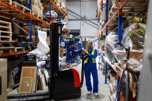 Wide shot of a warehouse worker standing with a forklift in the back of an auction warehouse. She is wearing a blue jumpsuit and yellow high-visibility jacket. She is surrounded by various antiques while she is looking directly at the camera.

Videos are available similar to this scenario.
