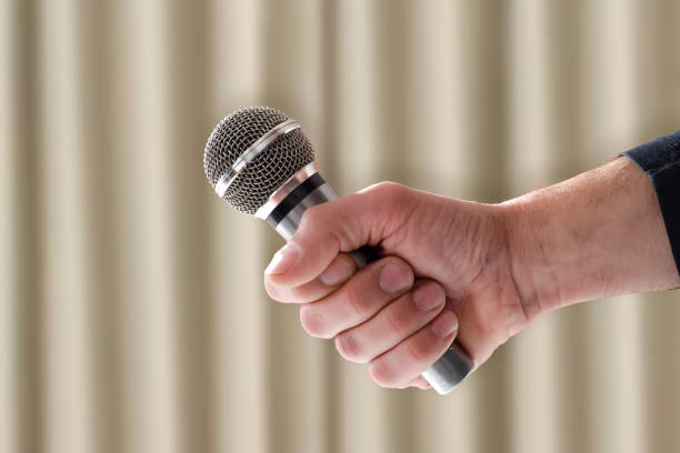 Female hand on blurred light background holding microphone for karaoke.Copy space.