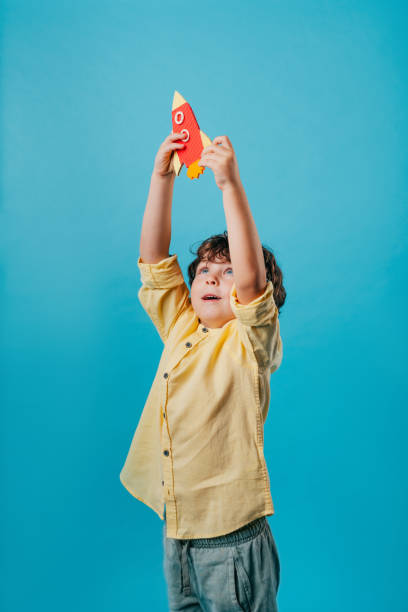 istock Little boy holding paper rocket toy standing over blue background 2190799412