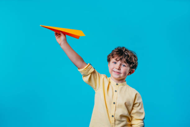 istock Little boy holding paper plane standing over blue background 2190799447