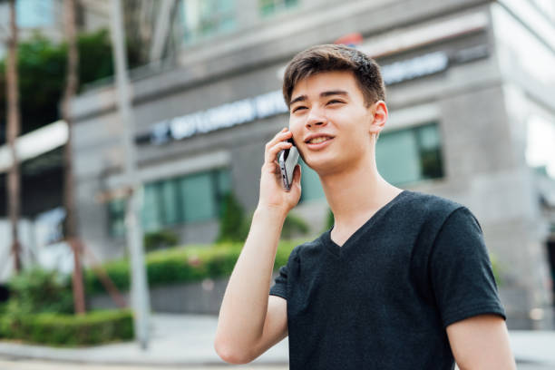 istock Young man in a striped shirt smiling while talking on a smartphone outdoors with green foliage in the background 2190799645