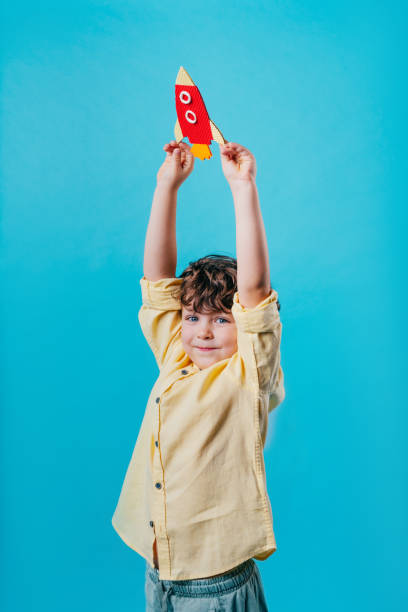 istock Little boy holding paper rocket toy standing over blue background 2190799954