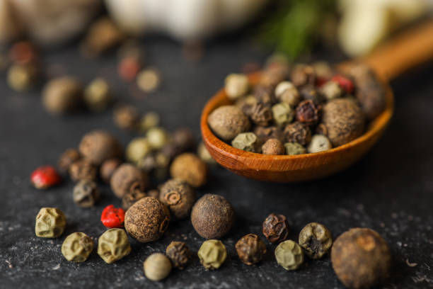 istock Close-up of a wooden spoon filled with assorted peppercorns on a dark textured surface, with garlic bulbs and rosemary in the background. Perfect for culinary and food concept themes 2190801210