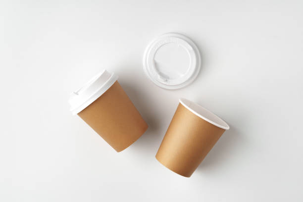 istock Two brown disposable coffee cups with white lids and a lid resting beside them on a clean white surface 2190802698