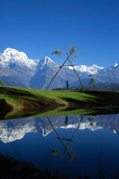 A young boy enjoys swinging on a traditional 'linge ping' swing during the Dashain festival in Nepal, with the breathtaking Mount Annapurna towering in the background. During Dashain, one of the most significant festivals in Nepal, people set up swings in villages and towns as a part of the celebrations, symbolizing joy, renewal, and the victory of good over evil. The vibrant cultural tradition is a way for communities to come together and celebrate, set against the stunning backdrop of the Himalayan peaks.