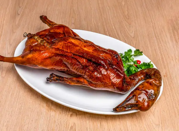 Roasted Goose Whole with coriander served in tray dish isolated on wooden table side view of hong kong food Roasted Goose Whole with coriander served in tray dish isolated on wooden table side view of hong kong food