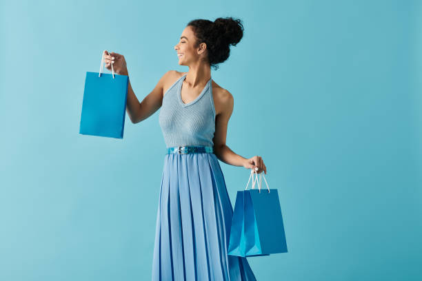 Young woman enjoys shopping while smiling against a bright blue background