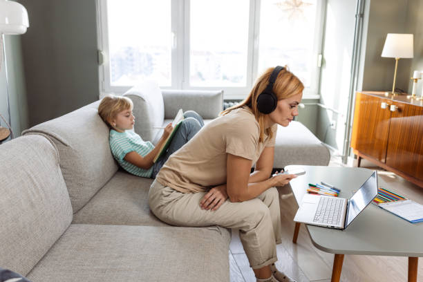 istock Mother working on laptop while daughter doing homework in cozy living room 2190807349