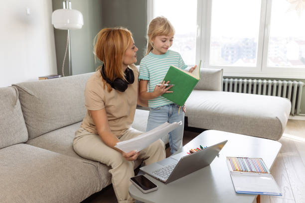istock Mother assisting young daughter with homework while working from home on a laptop 2190807356