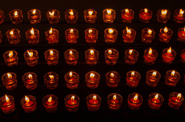 A multitude of small glass candles burns brightly in rows, casting a soft glow in a dim environment. The ambiance feels peaceful and reflective, ideal for meditation or remembrance.