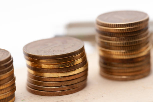 Heaps of money or pile of gold colored golden currency coins arranged as mountain or set or stacks of abundant money placed on a wooden surface over beige gray colored horizontal background with copy space