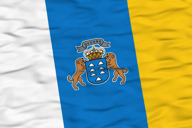 The flag of the Canary Islands, featuring three vertical stripes of white, blue, and yellow with the regional coat of arms in the center, is shown waving in the wind. The textured fabric conveys motion and symbolizes regional pride and identity.