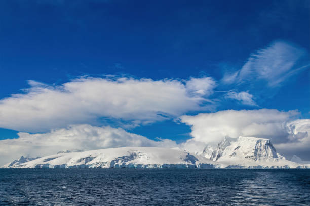 istock Snow covered coastline, Antarctica. Ocean in foreground. Blue sky, clouds overhead. 2190829503