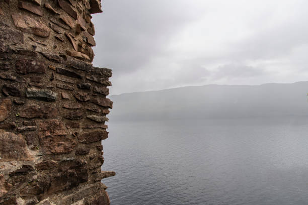 Drumnadrochit, Scotland, UK-18 June 2024; Close up of stone wall of ruined Urquhart Castle in the Highlands of Scotland besides foggy Loch Ness lake and mountains in background
