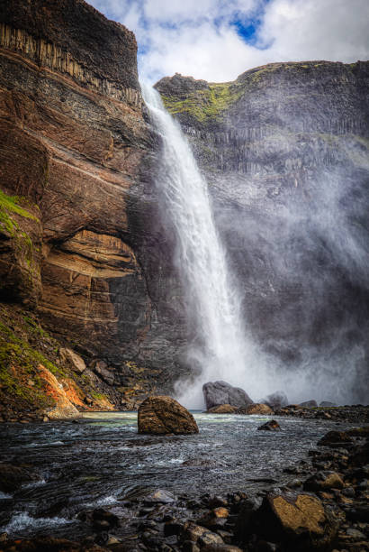 A striking image of Haifoss waterfall plunging over basalt cliffs in Iceland’s Highlands, shrouding the surrounding landscape in mist. The composition features lush green foliage contrasted against rugged rock formations, showcasing the area’s natural beauty.