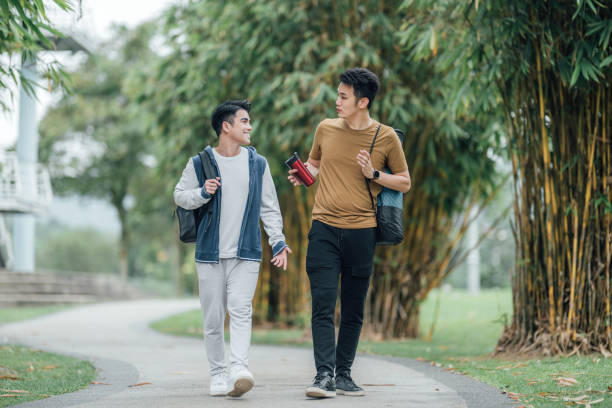 Two good Asian male friends walk and chat while strolling in a public park.
