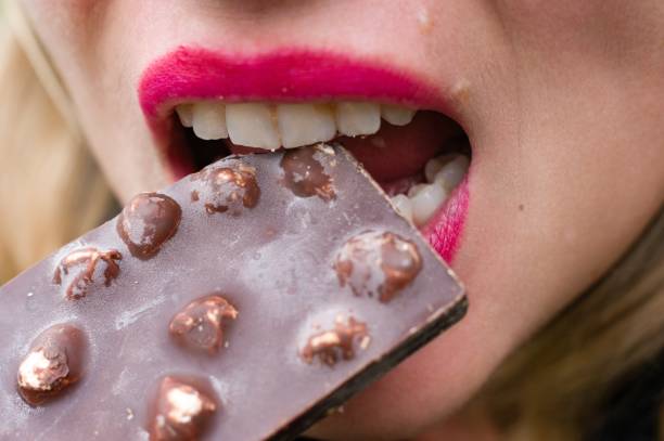 istock Woman biting into a chocolate bar with nuts 2190850831