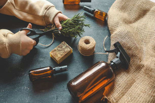istock Child's hands cutting a bundle of rosemary with scissors on a dark surface surrounded by amber glass bottles, burlap, natural soap, and twine. Rustic and eco-friendly crafting setup with herbal elements 2190850961