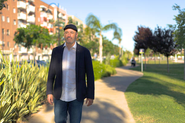 Serious man with ascot cap walking calmly through the park in the city at sunset