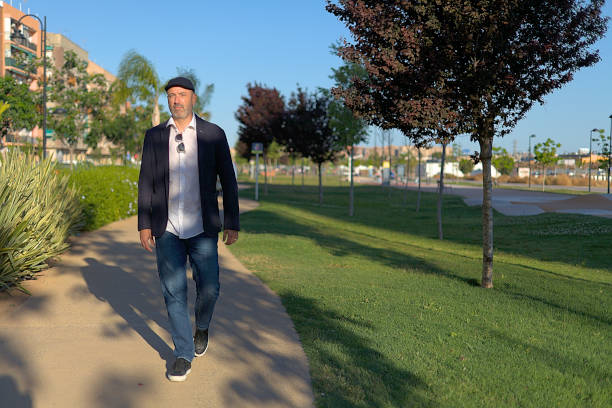 Serious man with ascot cap walking calmly through the park in the city at sunset