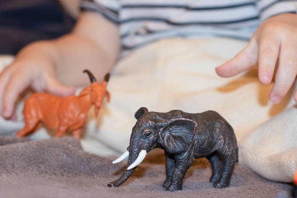 A child plays with a small black toy elephant and a toy red deer.