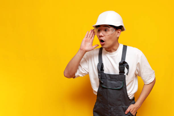 istock asian male builder in uniform announces information on yellow isolated background 2190863787