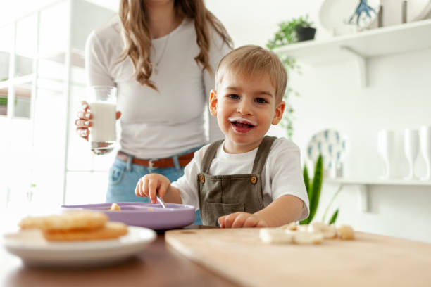 istock funny little boy 2 years old eats breakfast himself in the kitchen with a dairy product, the child is dirty with food 2190863855