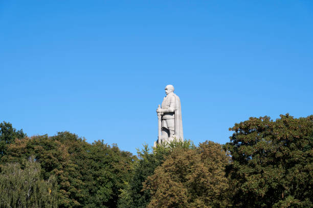 The imposing statue of Otto von Bismarck, Germany's first Chancellor and a key figure in German unification, stands tall above the tree line in Hamburg, Germany. Set against a clear blue sky, this iconic monument captures Bismarck in a commanding pose, symbolizing strength and national pride.