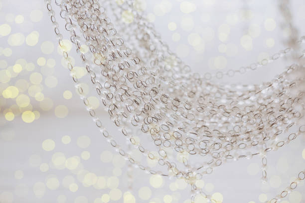 Delicate chains hang gracefully, creating a shimmering effect against a soft golden bokeh backdrop. The atmosphere evokes a festive mood, perfect for celebrating Christmas and New Year.